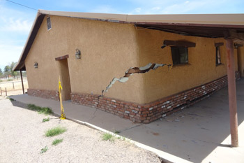 A house with a broken window and a brick wall, showing structural damage