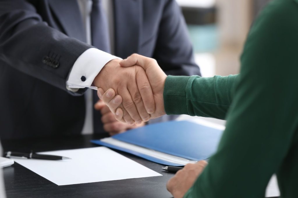 Two people shaking hands over a desk, settling property damage claim successfully, with an adjuster present