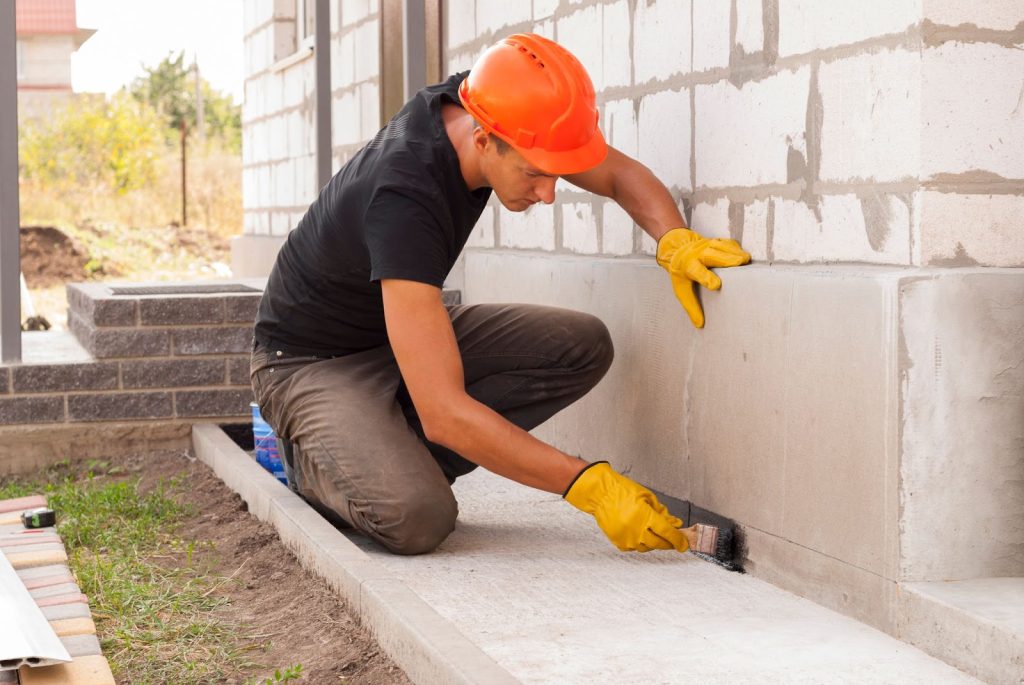 A man repairing a wall with cement due to foundation damage, foundation repair, and foundation problems.