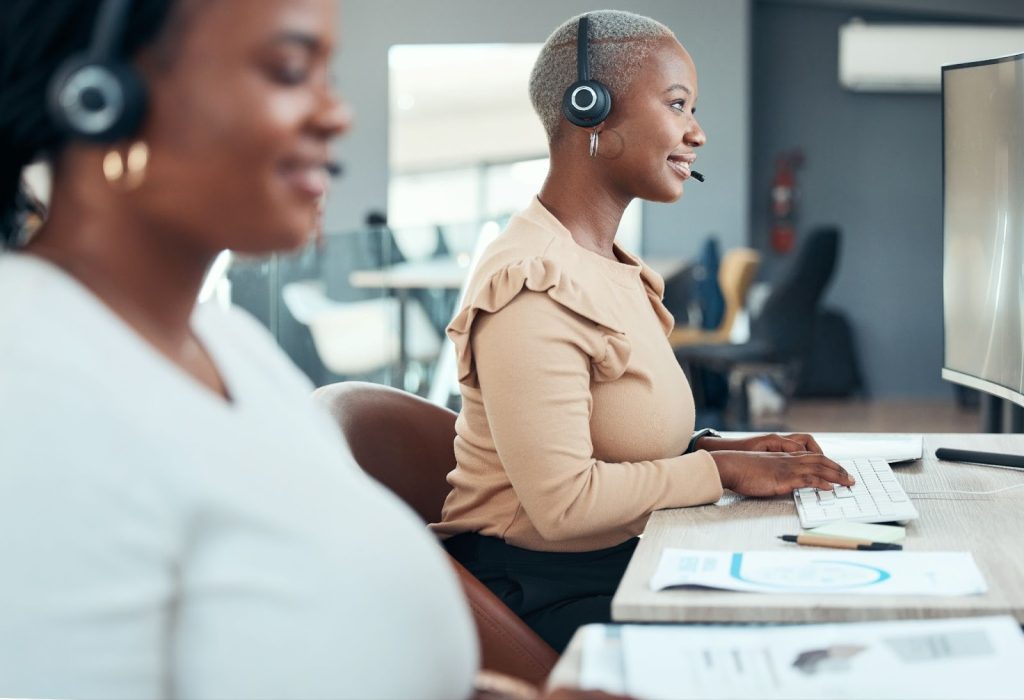 Two women wearing headsets while working at a computer.