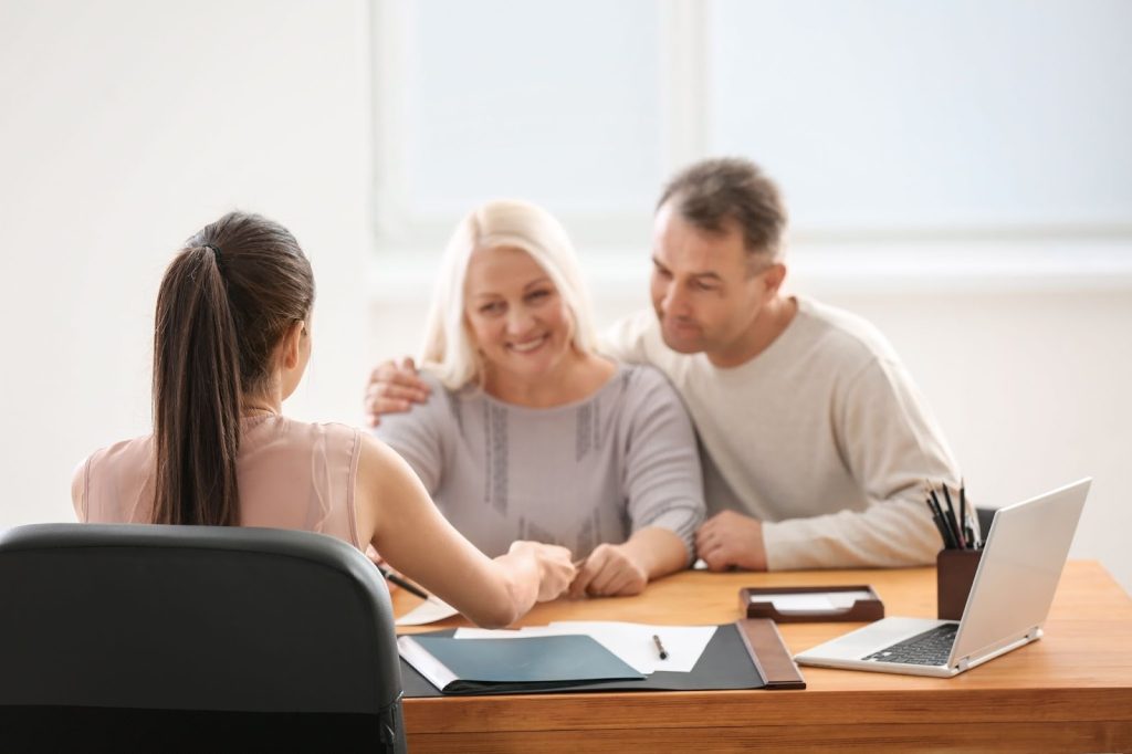 A man and woman, both public adjusters, collaborate at a desk with a laptop, discussing insurance claims and strategies.