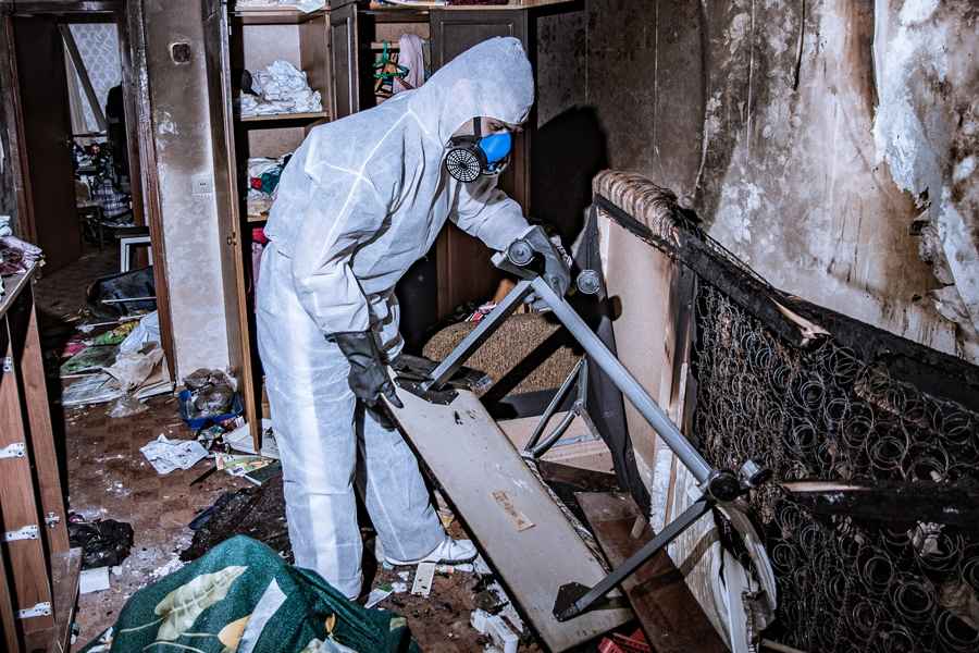 A man in a white suit and protective gear cleans a room, representing Hudson Douglas Public Adjusters' commitment to safety.