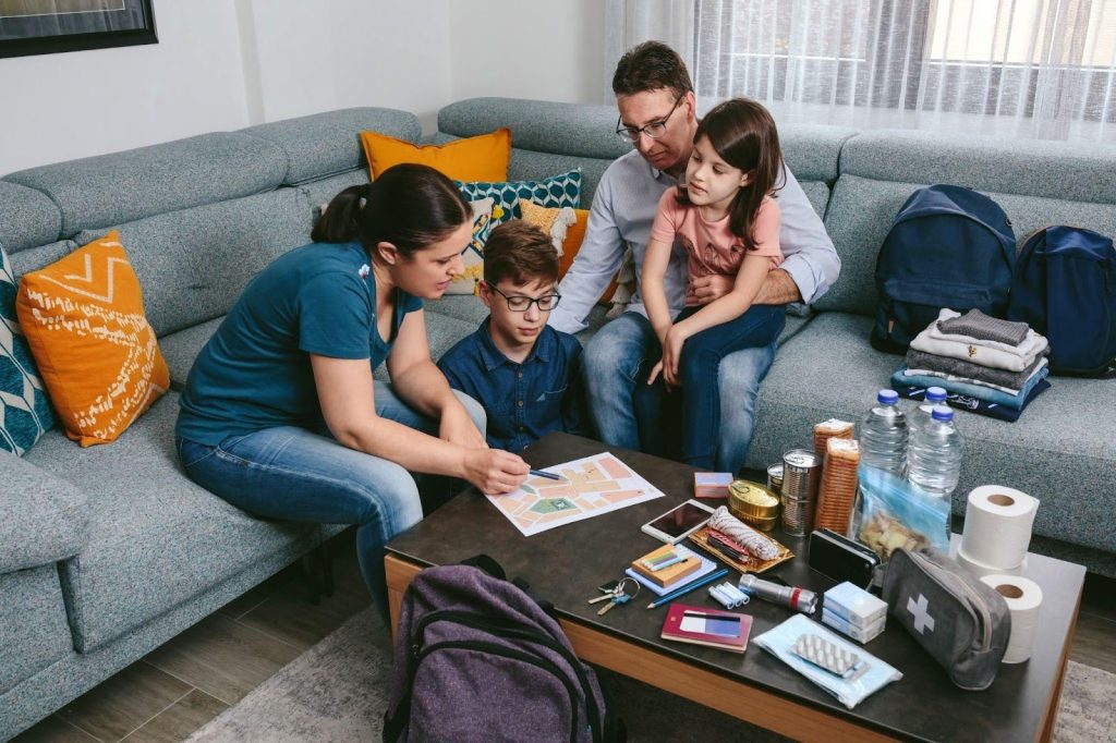 A family of four sits on a couch surrounded by their luggage preparing for a trip together
