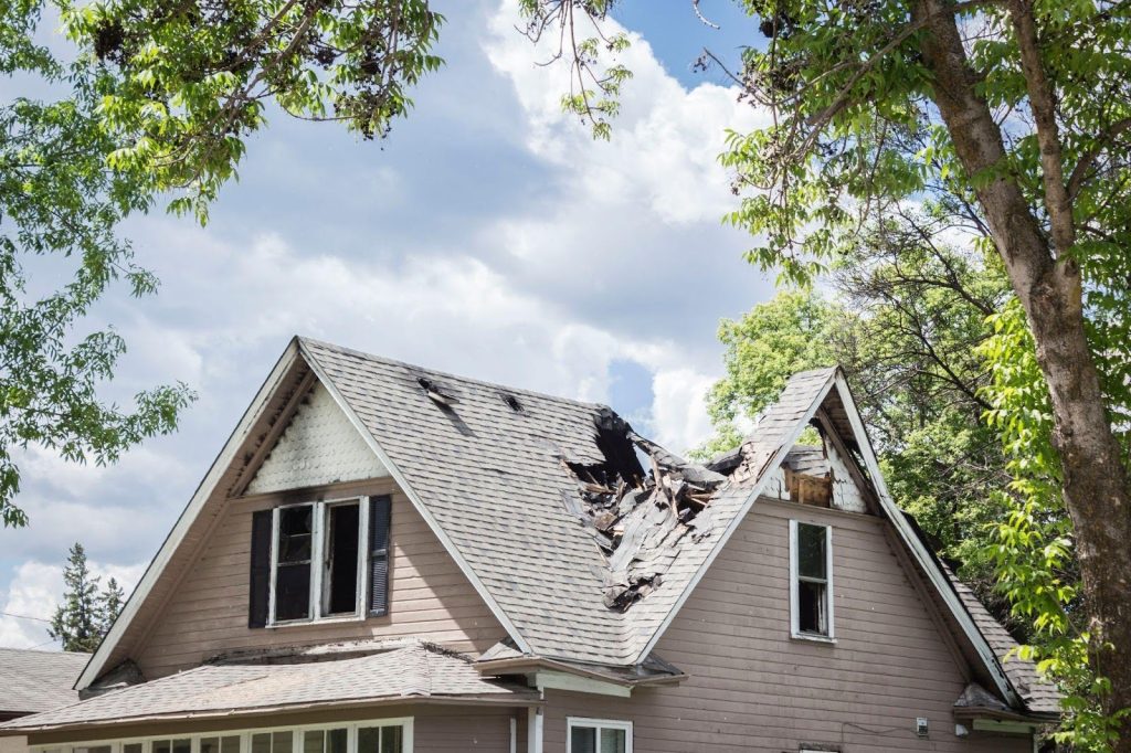 A house with a visibly damaged roof showing signs of wear and potential structural issues