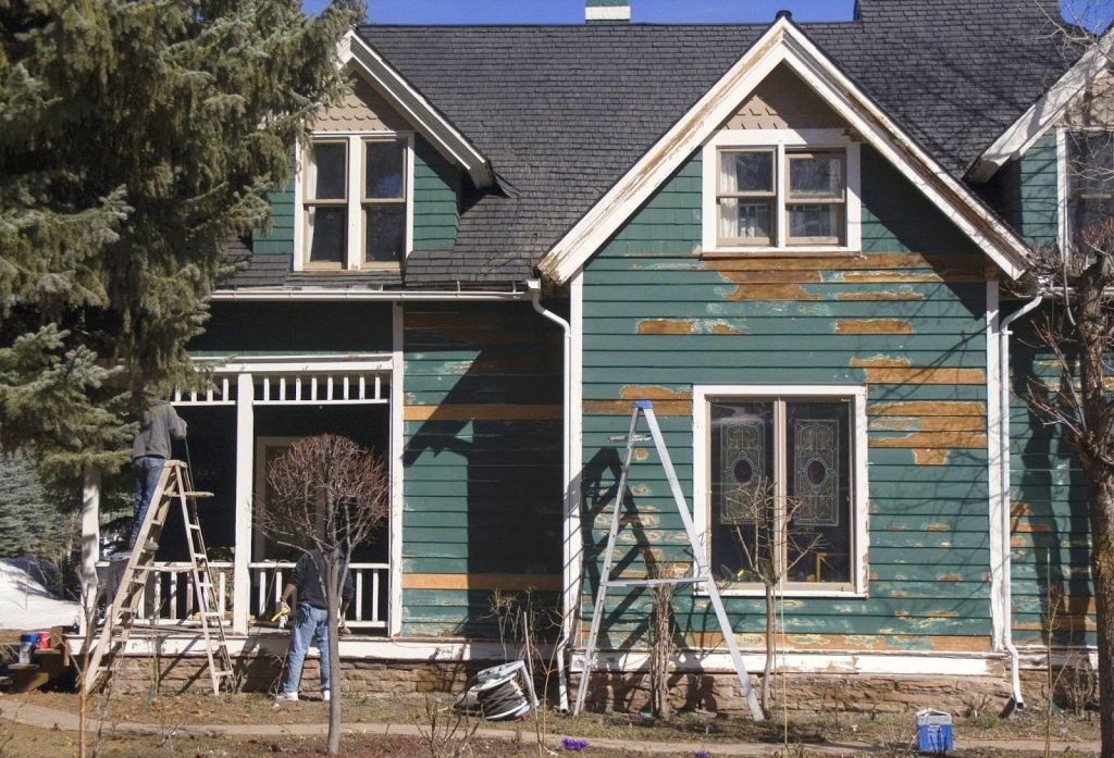 A green-painted house with a ladder leaning against it set against a clear blue sky